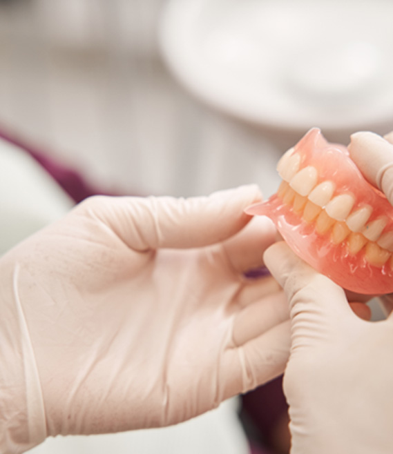 Gloved hands holding full set of dentures