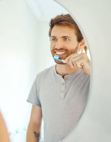 Man brushing his teeth in front of bathroom mirror