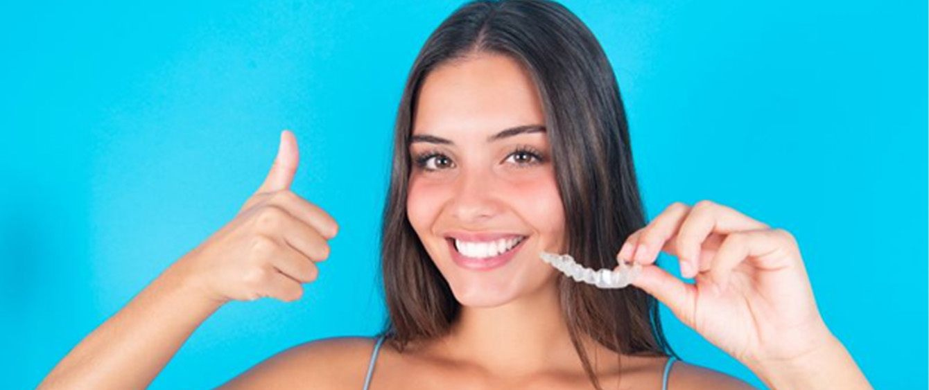 Woman holding Invisalign aligner, making thumbs-up gesture