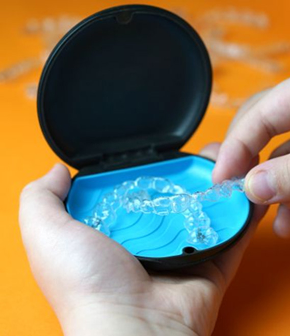 Person removing clear aligner from its storage case