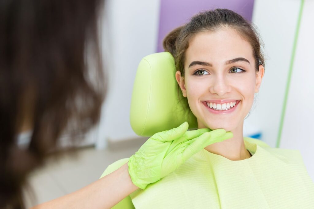 Teenager in green dental chair with dentist touching her face with green glove
