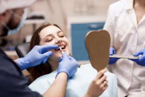 Patient in dentist’s chair looking into handheld mirror and dentist about to place veneer.